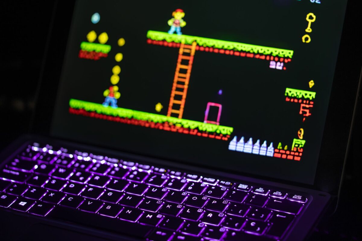 Close-up of a laptop displaying a retro video game with a neon-lit keyboard, capturing the nostalgic gaming experience.